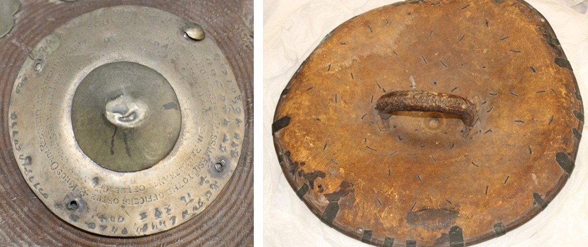 Two photos: 1. close-up of the metal shield boss with an Ethiopic inscription around the outer rim and an English inscription within. 2. the reverse of the shield: brown hide dotted with flattened nails holding it to the metal front, and a sturdy handle in the centre.